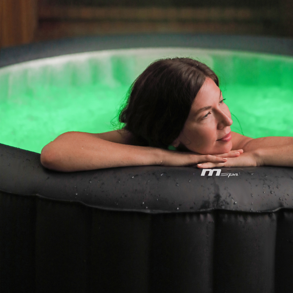 Person resting against the edge of a hot tub illuminated with green lighting
