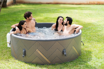 Four adults enjoying the MSpa MONO inflatable hot tub on a green backyard lawn
