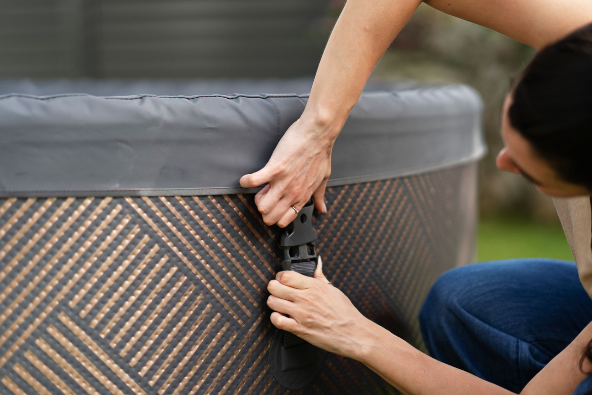 Close-up of a person fastening the secure buckle closure on the MSpa MONO 6-person inflatable hot tub cover