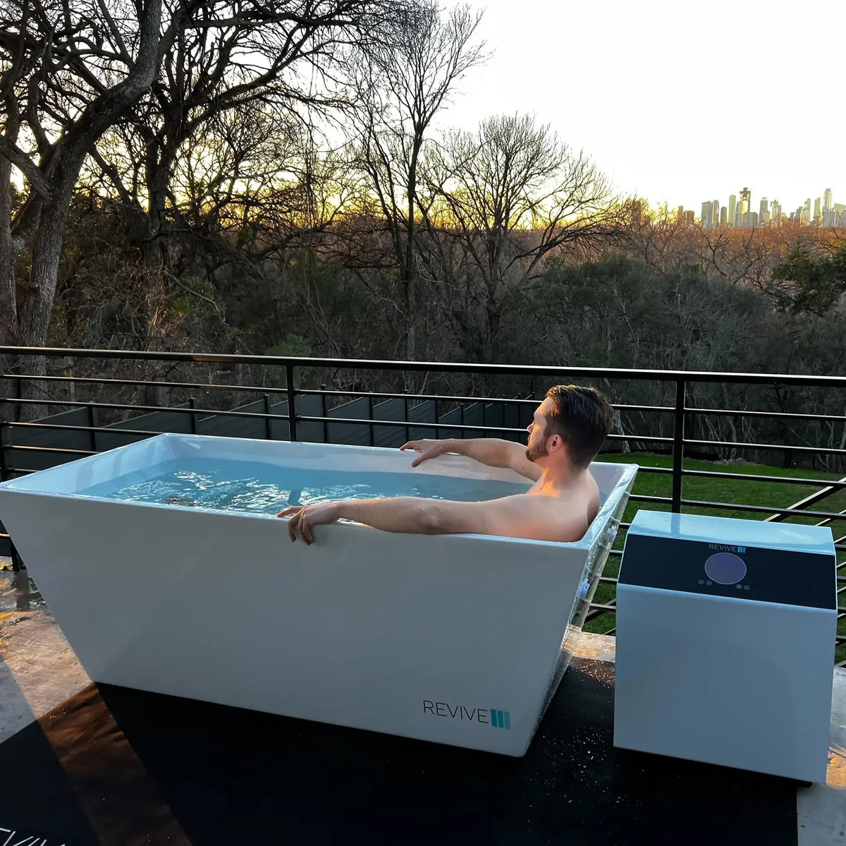 Person using a white Revive acrylic cold plunge outdoors beside the external chiller