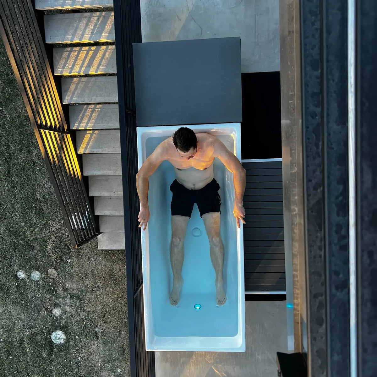 Overhead view of a person seated in the rectangular Revive acrylic cold plunge filled with blue water